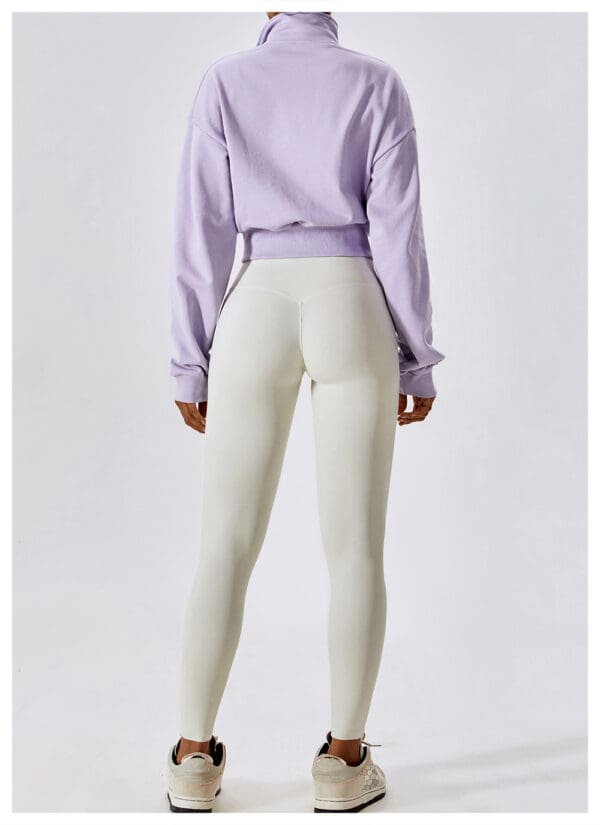 A woman wearing white pants and a purple sweatshirt.