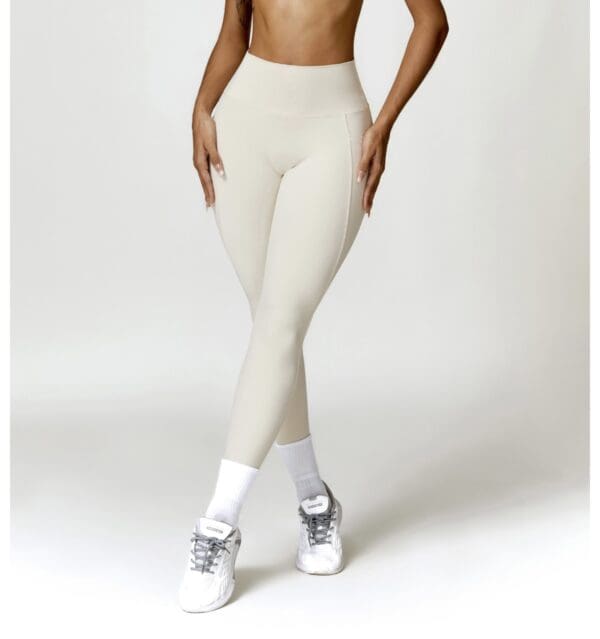 A woman wearing white pants and sneakers is standing.