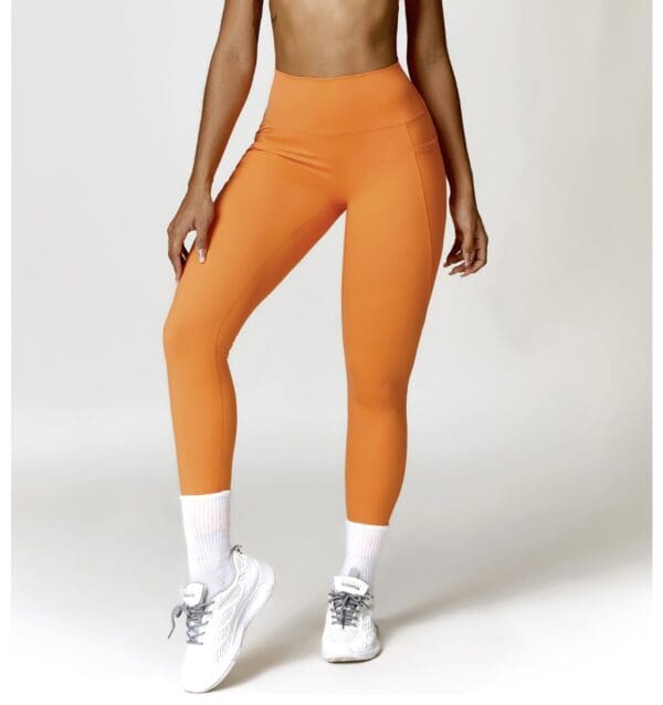 A woman wearing orange leggings and white sneakers.